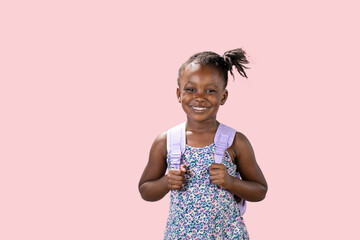 ritratto in studio con sfondo rosa di una piccola ragazza felice che indossa lo zaino per la scuola