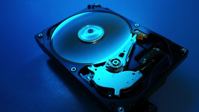 Disassembled hard drive works in blue light in the dark, close up. Hard disk from the inside. Broken tightness of the hard drive. HDD repair, Data Recovery.