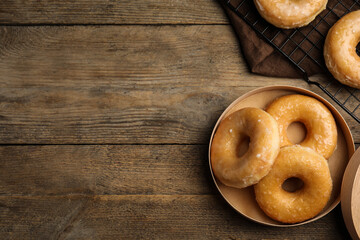 Delicious donuts in box on wooden table, flat lay. Space for text