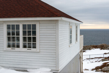 The exterior of a white wooden clapboard building with two glass windows, a black roof, and a...