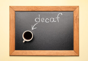 Chalkboard with word decaf and cup of coffee on beige background, top view