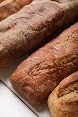 Different tasty baguettes on white wooden table, closeup