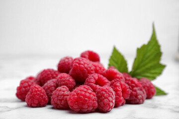 Fresh ripe raspberries with green leaves on white marble table, closeup