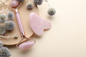 Flat lay composition with rose quartz gua sha tool and facial roller on beige background. Space for...