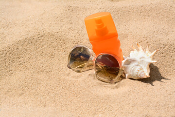 Fototapeta na wymiar Bottle with sun protection spray, sunglasses and seashell on sandy beach, space for text