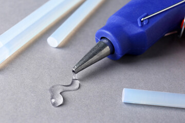 Melted glue dripping out of hot gun nozzle near sticks on grey background, closeup