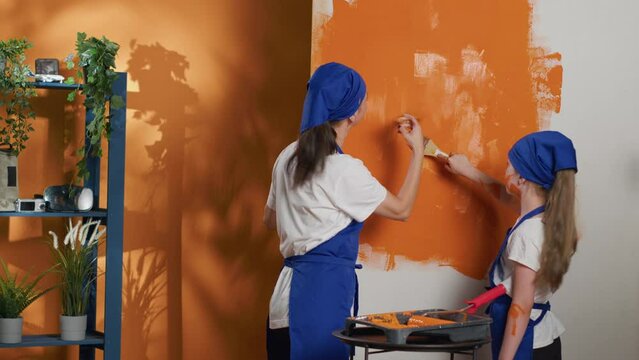 Young people painting apartment walls with orange color, using renovating tools to redecorate house interior. Using paint and paintbrush or diy equipment to renovate room at home. Tripod shot.