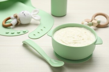 Plastic dishware with healthy baby food on white wooden table. Space for text
