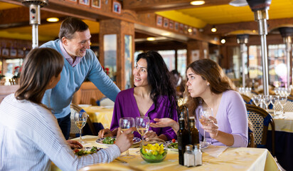 Polite smiling adult man getting acquainted with group of women having lunch in cozy restaurant