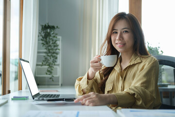 Happy young businesswoman drinking coffee and working at bright office.