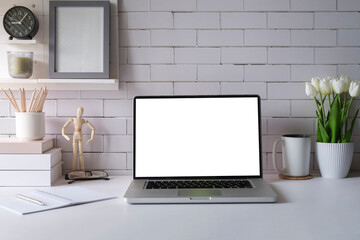 Laptop with empty screen, picture frame, flower pot and supplies on white table.