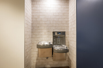 Two water fountains in an insert in a wall. One is placed higher than the other that has optical system for filling up bottles and counting how many plastic containers are saved. - obrazy, fototapety, plakaty