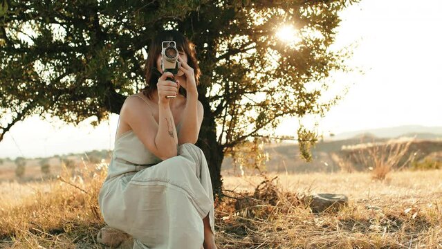 Girl shoots video with super 8 vintage tape camera under the tree in the nature