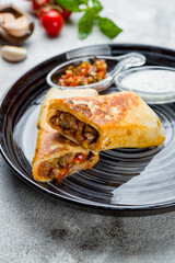 Mexican burrito with meat, vegetables,corn and red beans on plate with sour cream and tomato salsa sauce, vertical