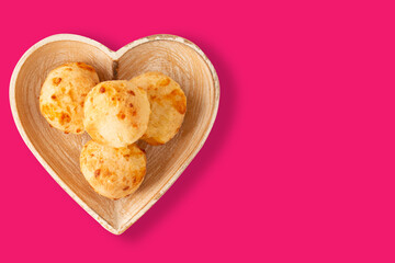 Cheese bread (Brazilian pao de queijo mineiro), top view, pink background, on a heart shaped plate.