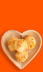 Cheese bread (Brazilian pao de queijo mineiro), top view, orange background, on a heart shaped plate, vertical