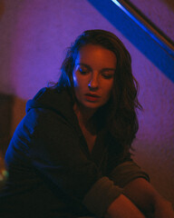 Girl with a cigarette at night sits against the background of neon light