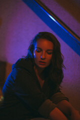 Girl with a cigarette at night sits against the background of neon light