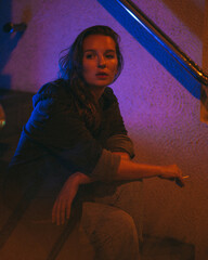 Girl with a cigarette at night sits against the background of neon light