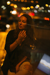 A girl walks around the city at night after the rain among the light of lanterns and cars