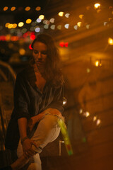 A girl walks around the city at night after the rain among the light of lanterns and cars