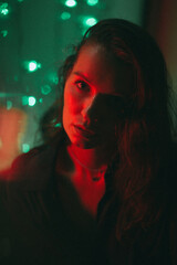 A girl sits at a colorful shop window at night