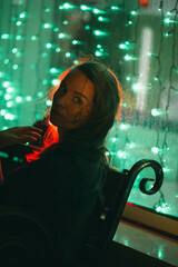 A girl sits at a colorful shop window at night