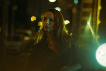 A girl walks around the city at night after the rain among the light of lanterns and cars