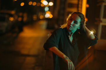 A girl walks around the city at night after the rain among the light of lanterns and cars