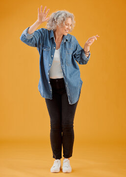 Fun, Happy And Cheerful Woman Dancing, Celebrating And Enjoying Life Alone Against An Orange Background. Senior Woman Feeling Excited, Joyful And Playful With Dressed Stylish, Trendy And Fashionable