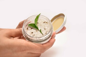 A girl Holding a bottle of cosmetic. The scrub is made out of tea leaves and sea sault. 