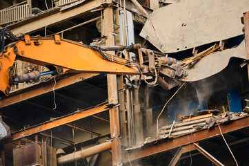 Hydraulic scissors on rigging demolish industrial building