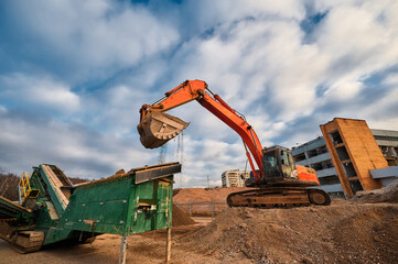A construction excavator loads crushed stone into the receiving hopper of a mobile crushing and sorting complex. - obrazy, fototapety, plakaty