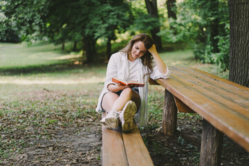Woman holds book in her hands. Reading the book sitting on a bench at outdoors