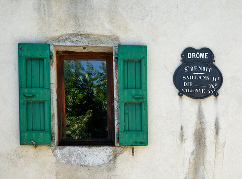 A window with green shutters and an old distance sign on a wall in St-Benoit-en-Diois in the Drome department, showing distances to Saillans, Die and Valence.