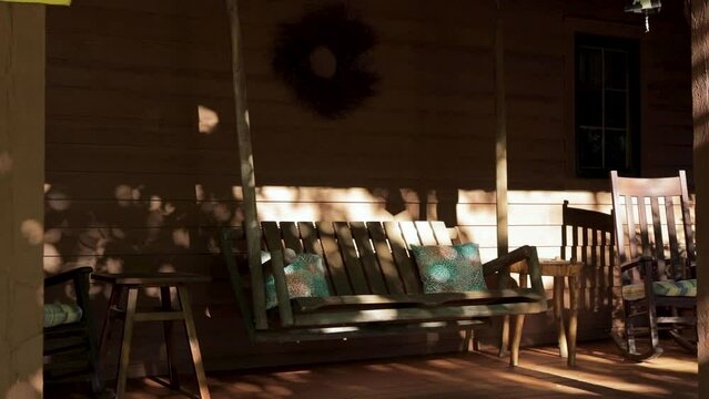 Wooden front porch swing swaying in the morning sun light. 