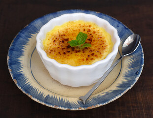 Creme brulee in a ceramic bowl on wooden table and black background