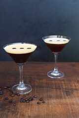 Glasses of espresso martini with coffee beans on wooden table and black background