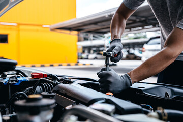Mechanic using wrench while working on car engine at garage workshop.