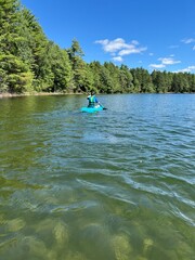 Fototapeta na wymiar boy paddles kayak away from camera on a clear water lake with forest shoreline in northern wisconsin