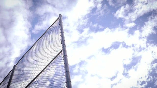 Edge of a Baseball Batting Cage Fence against Blue Sky with Clouds