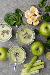 Healthy green spinach smoothie in glass jars and other ingredients on a gray concrete background. Superfoods, detox, diet, healthy food. Celery, apple, spinach, spinach, and banana.
