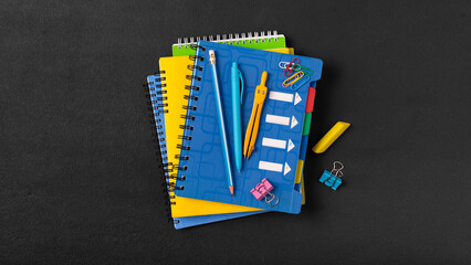 A stack of colored school notebooks and an alarm clock on a school chalkboard background. Back to school concept, banner