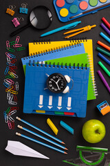 A stack of colored school notebooks and an alarm clock on a school chalkboard background. Back to school concept, banner