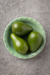 Three avocado fruits in a green plate on a gray table. Close-up, copy space for text