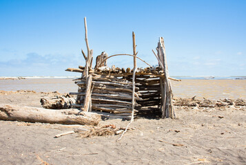 Beach hut made of sticks and driftwood on a sunny day in New Zealand