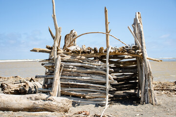 Beach hut made of sticks and driftwood on a sunny day in New Zealand