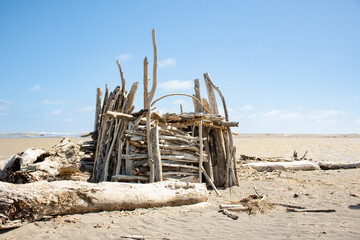 Beach hut made of sticks and driftwood on a sunny day in New Zealand