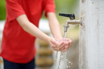 Closeup photo of child washing hands in a city fountain. Little boy drinking clean water from a street pump.