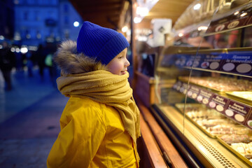 Little boy boy chooses sweets (fruit in chocolate glaze) on street Christmas market
